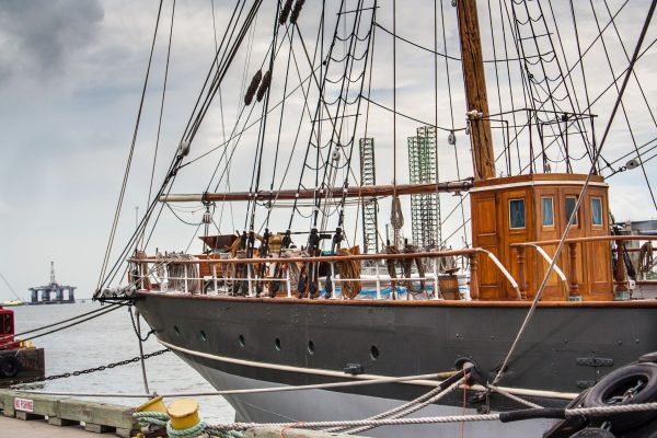 Wooden tall ship docked at a harbor with complex rigging and ropes on deck